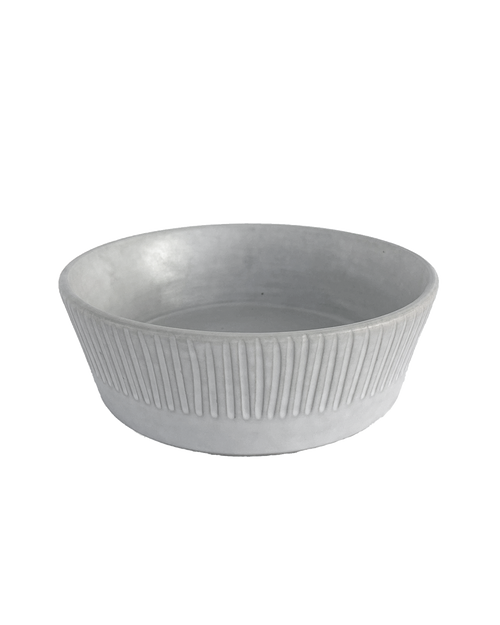 Carved matte white ceramic serving bowl with vertical lines around the outside on a black background