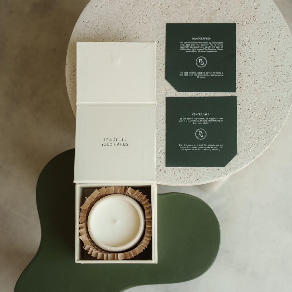 Sandalwood candle nestled in its open gift box with scent cards, shown from above on a green and stone ground
