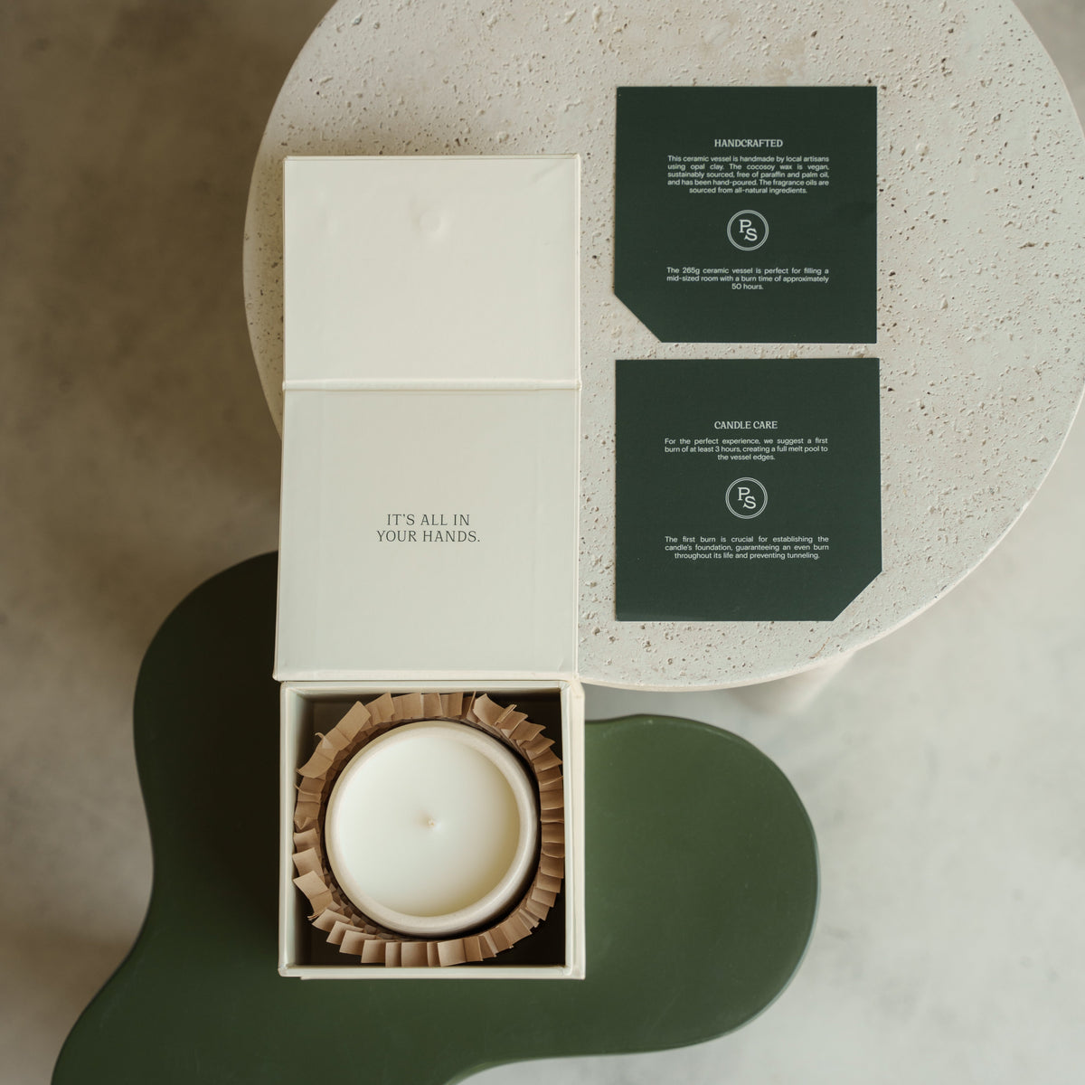 Neroli candle in its open gift box with dark green scent cards, shown from above on a stone and green ground