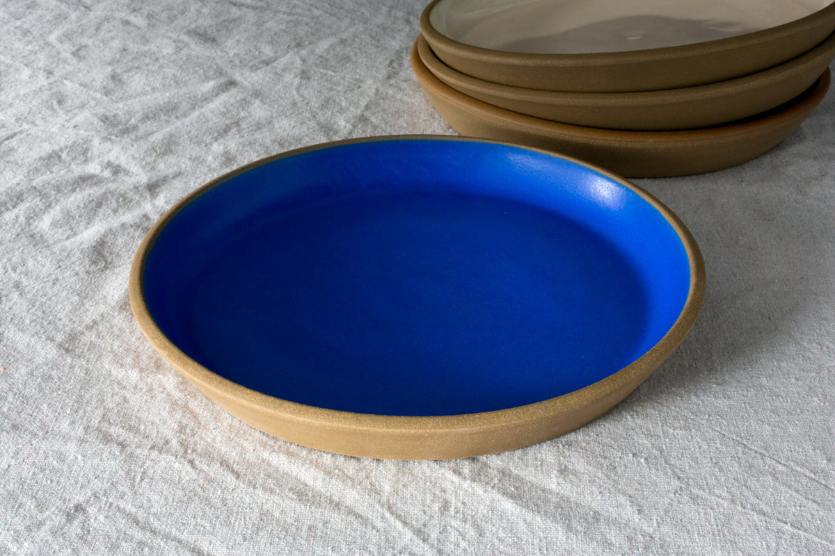 Fat Rim stoneware dinner plate in a matte cobalt blue glaze with a bare clay rim on a white linen cloth
