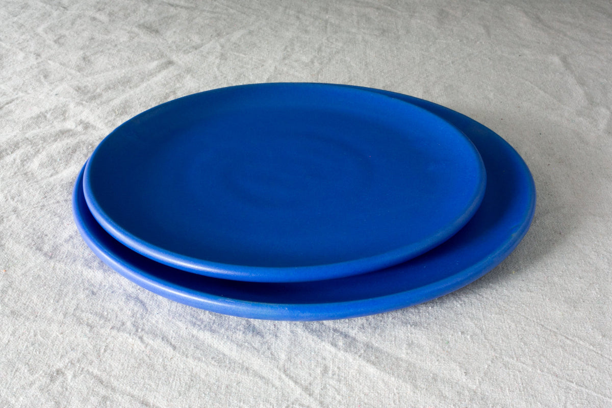 Horizon stoneware lunch plate in matte cobalt blue resting on a larger matching plate on white linen