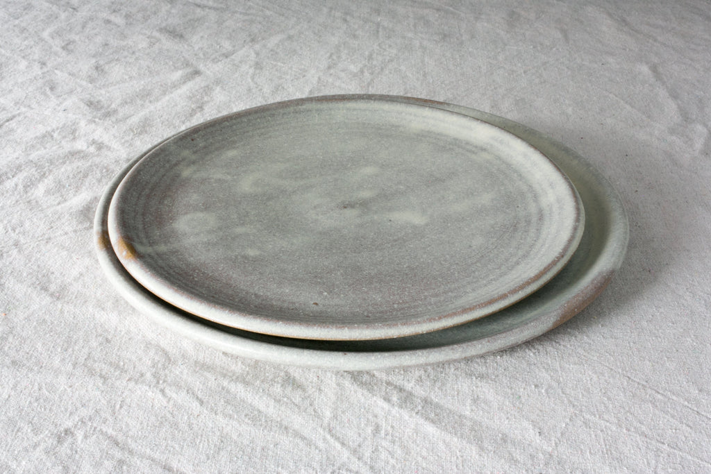 Horizon stoneware lunch plate in a pale speckled oat glaze sitting on a larger matching plate on linen