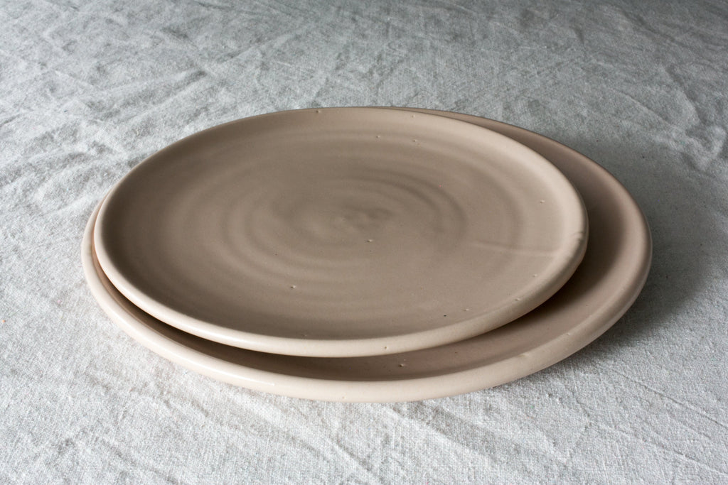 Two Horizon stoneware dinner plates in a soft satin sand glaze stacked on a rumpled white linen cloth