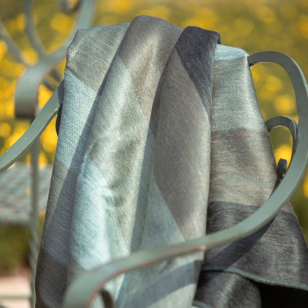 Green striped handwoven alpaca throw hanging over the back of an outdoor chair in soft sunlight