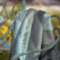Sage and green striped alpaca throw draped over a teal metal garden chair with yellow flowers behind