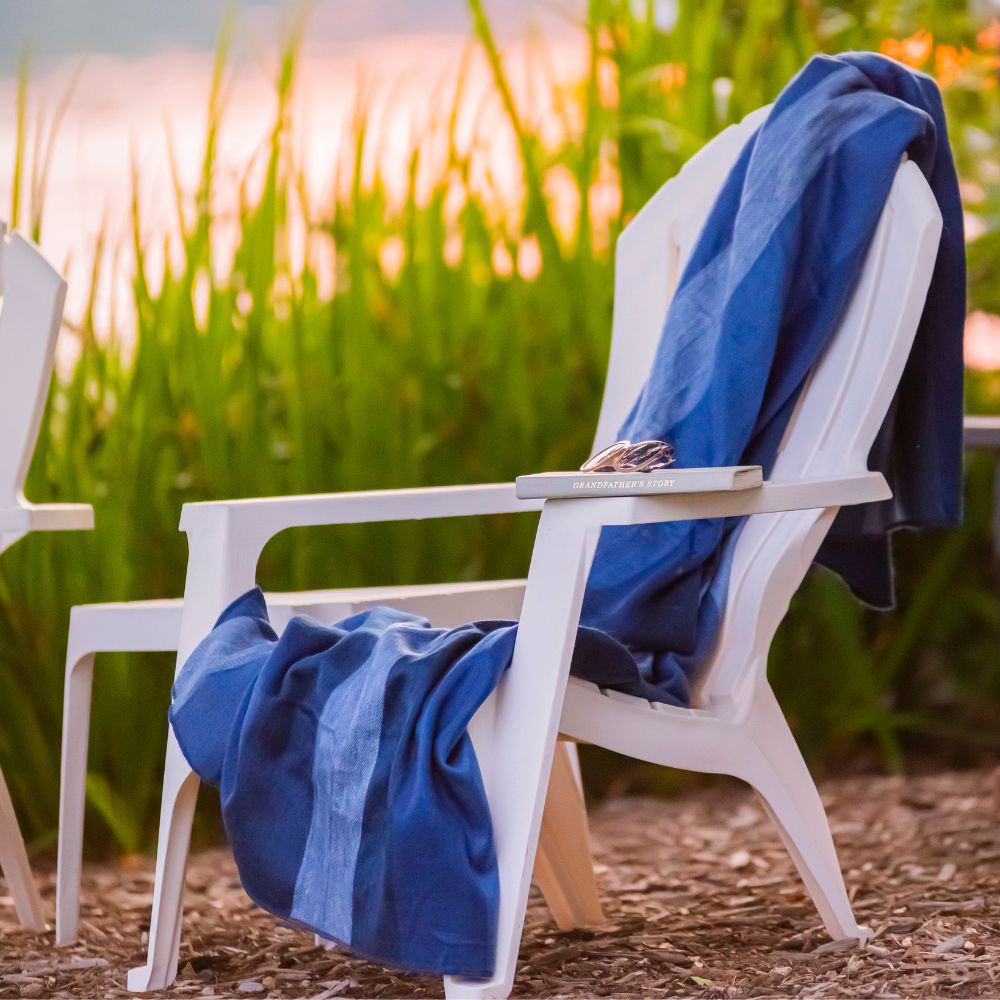Alpaca throw in denim and navy stripes draped over a white Adirondack chair in front of tall green grass