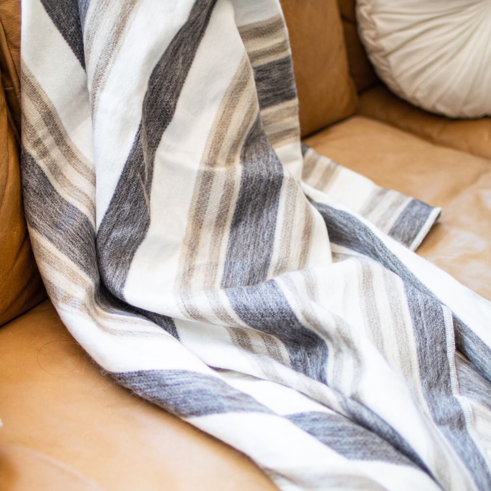 Cream, charcoal and camel striped alpaca throw draped over a brown leather sofa with a pale cushion