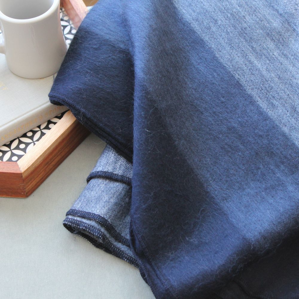 Close view of a folded alpaca throw in indigo and navy stripes beside a white mug on a tray
