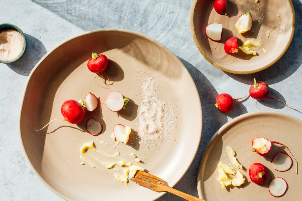 Horizon stoneware plates in a satin sand glaze with sliced radishes, butter and salt, seen from above