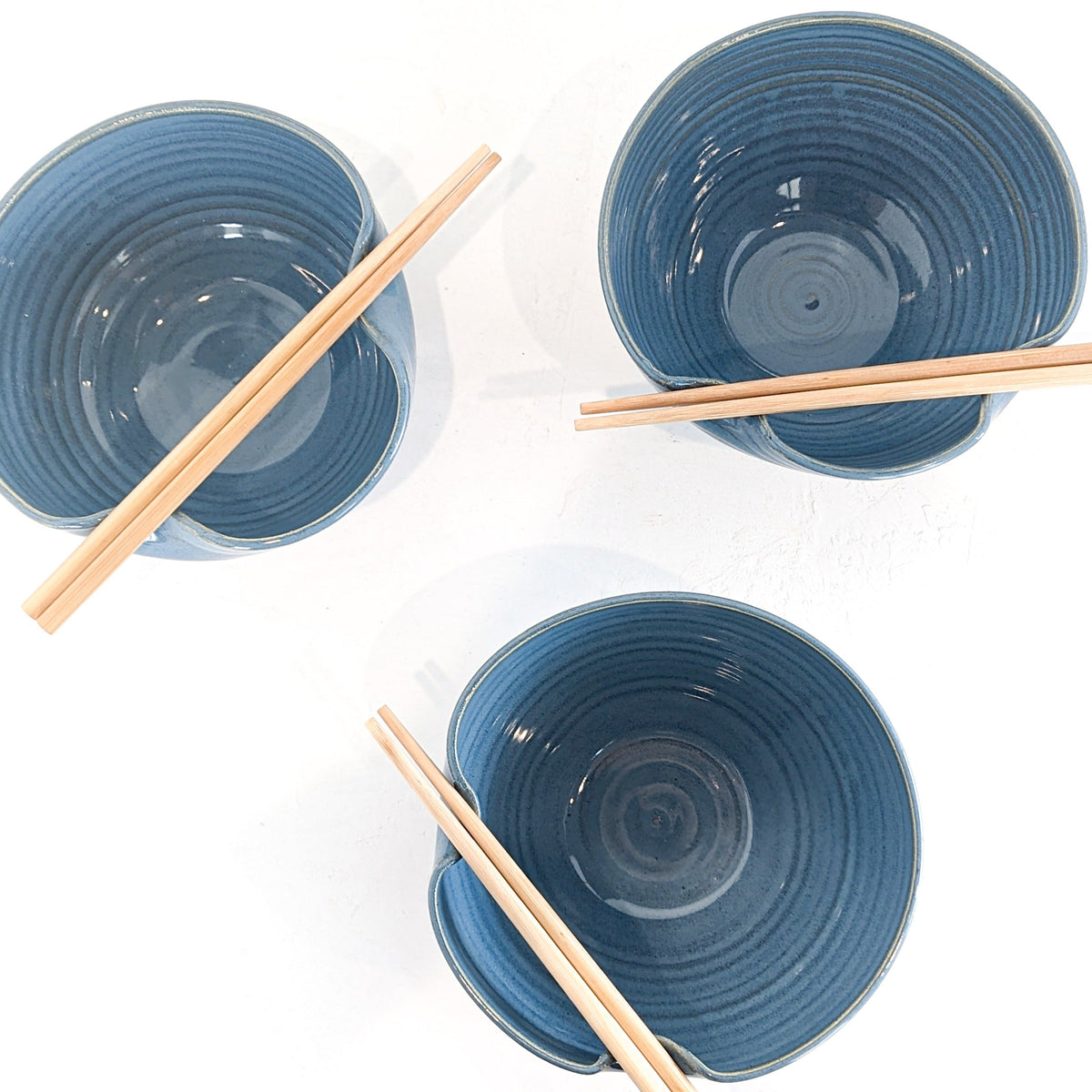 Three sky blue stoneware ramen bowls from above, each with a pair of chopsticks held by the folded rim