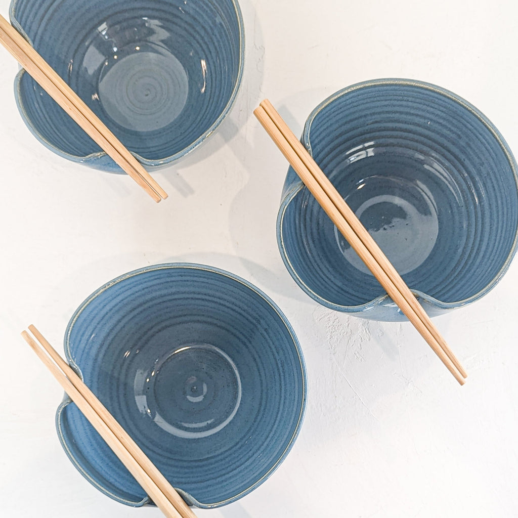 Overhead view of three hand-thrown sky blue stoneware ramen bowls with chopsticks resting across the rims