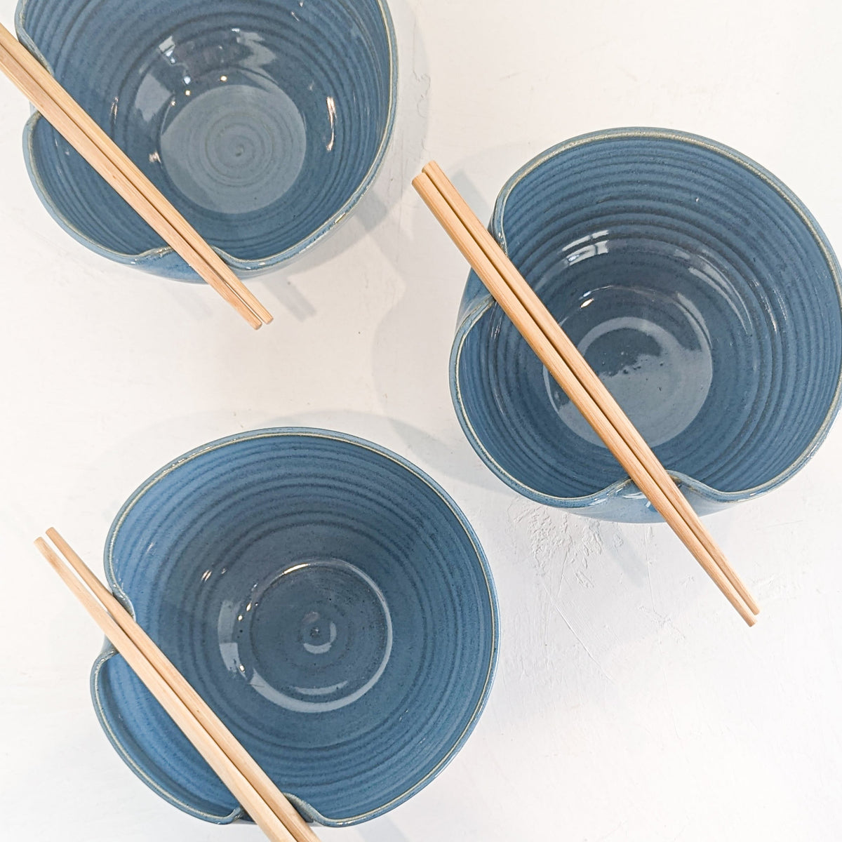 Overhead view of three hand-thrown sky blue stoneware ramen bowls with chopsticks resting across the rims