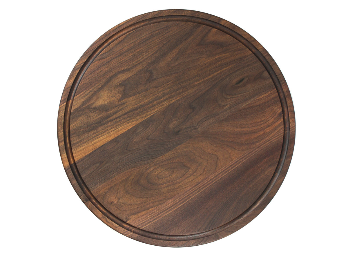 Round walnut cutting board, 18 in, with a juice groove, overhead view on white with dark swirling grain