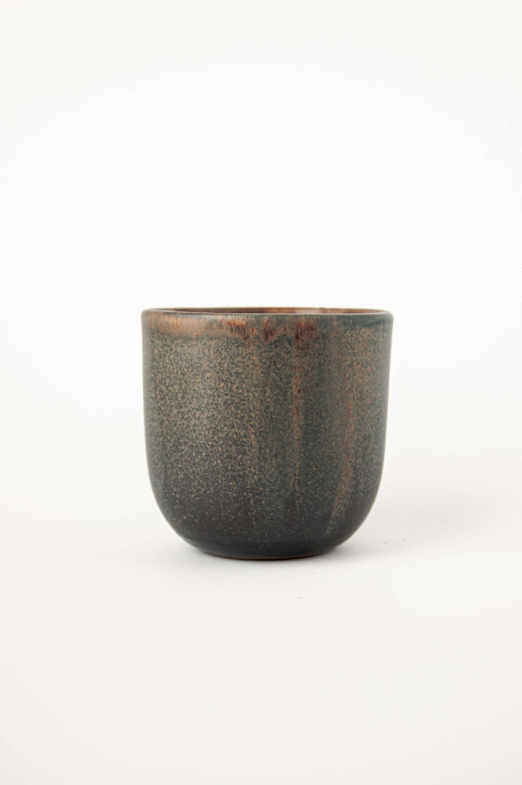Handleless stoneware coffee cup in speckled grey green glaze with rust drips at the rim, side view on white