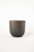 Handleless stoneware coffee cup in speckled grey green glaze with rust drips at the rim, side view on white