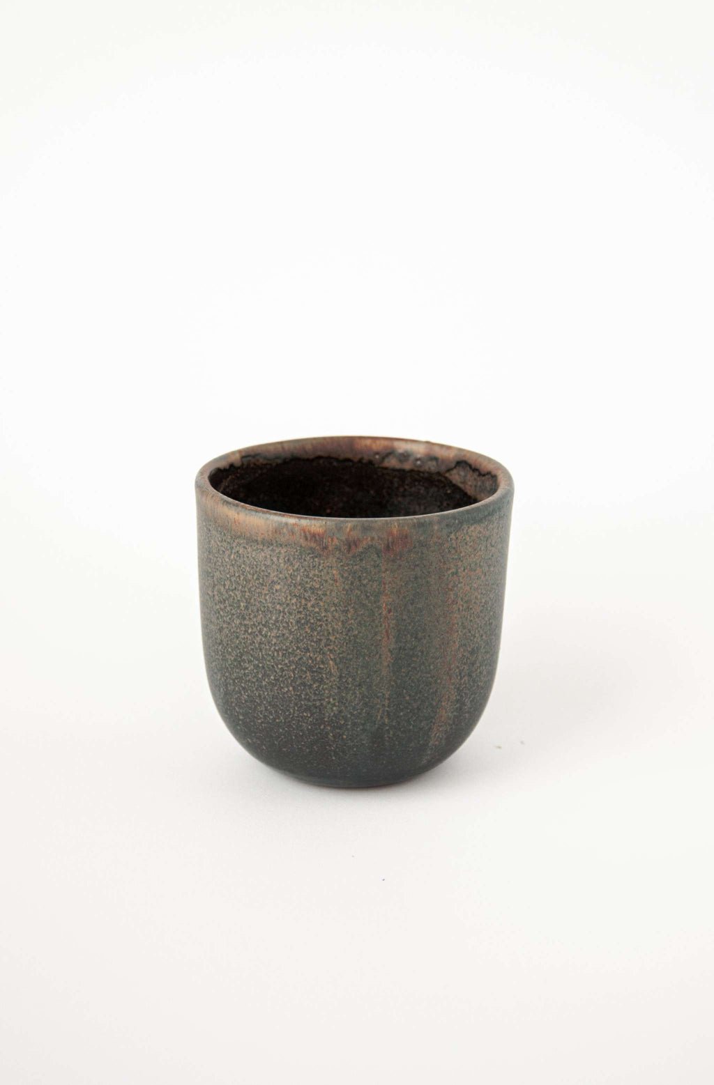 Handleless stoneware coffee cup in speckled glaze with a rust rim, angled view showing the dark interior
