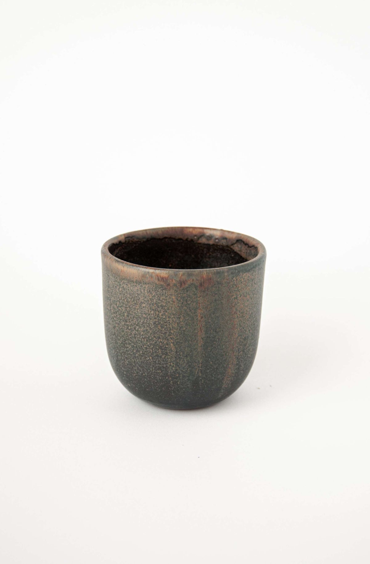 Handleless stoneware coffee cup in speckled glaze with a rust rim, angled view showing the dark interior