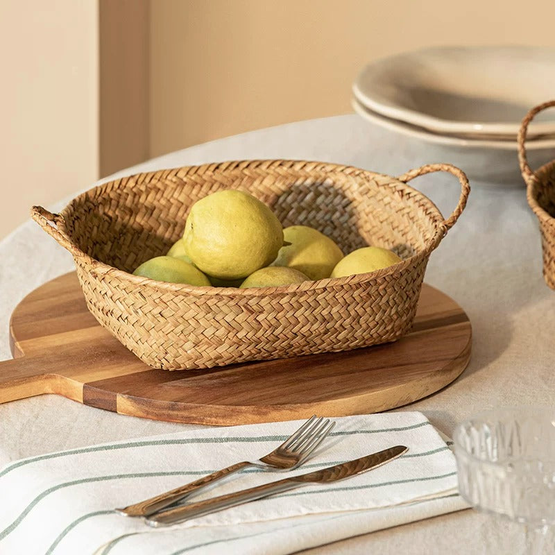Oval seagrass bread basket with loop handles holding green pears on a wooden board over a linen cloth