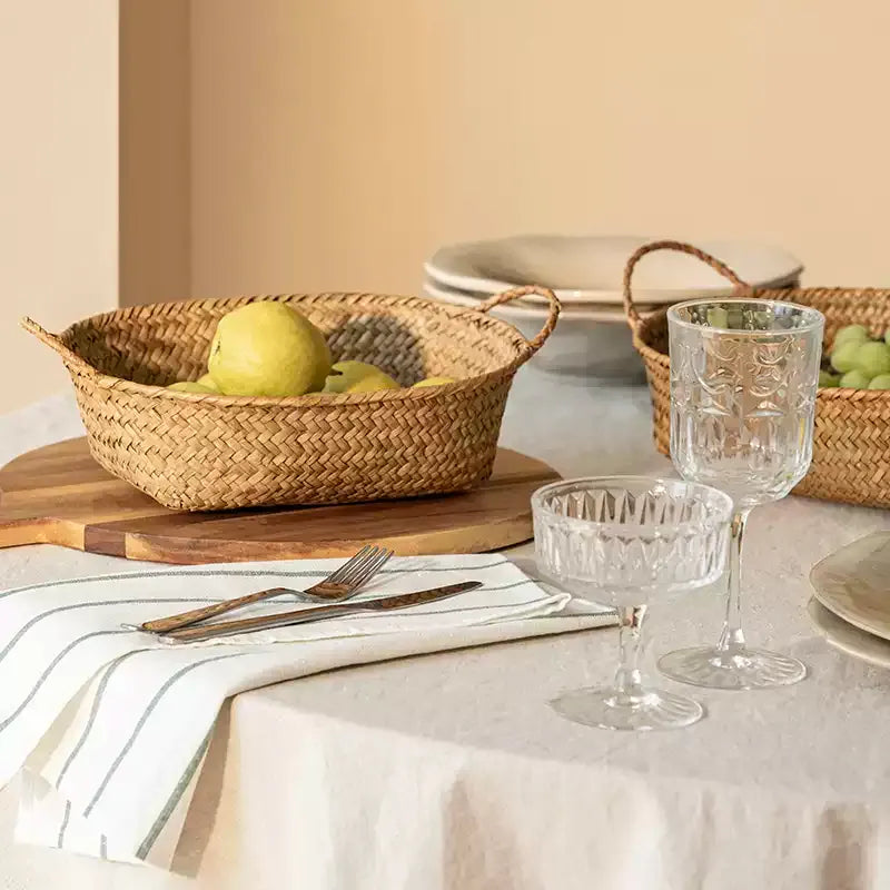 Oval seagrass basket in golden straw holding pears on a set table with cut glass stemware