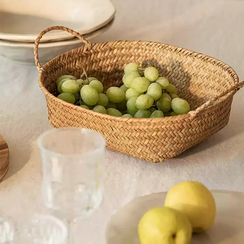 Shallow oval seagrass basket with handles filled with green grapes on a linen tablecloth