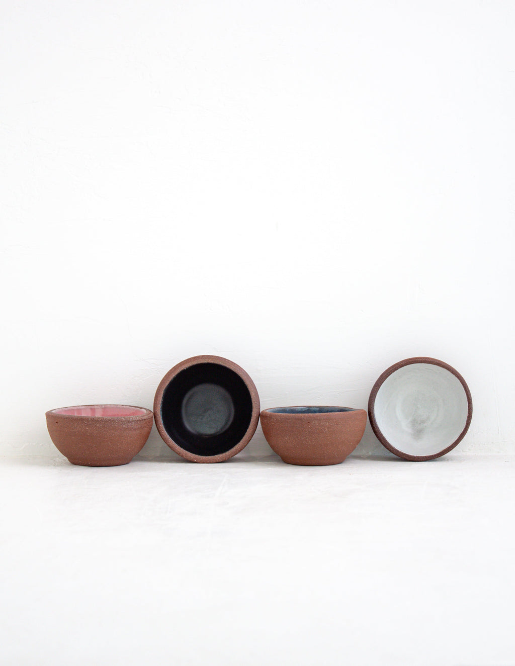 Four hand-thrown stoneware coupe sauce bowls in pink, black, sky blue and white glaze with red clay exteriors
