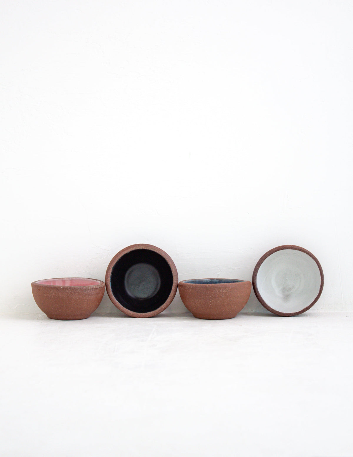 Four hand-thrown stoneware coupe sauce bowls in pink, black, sky blue and white glaze with red clay exteriors