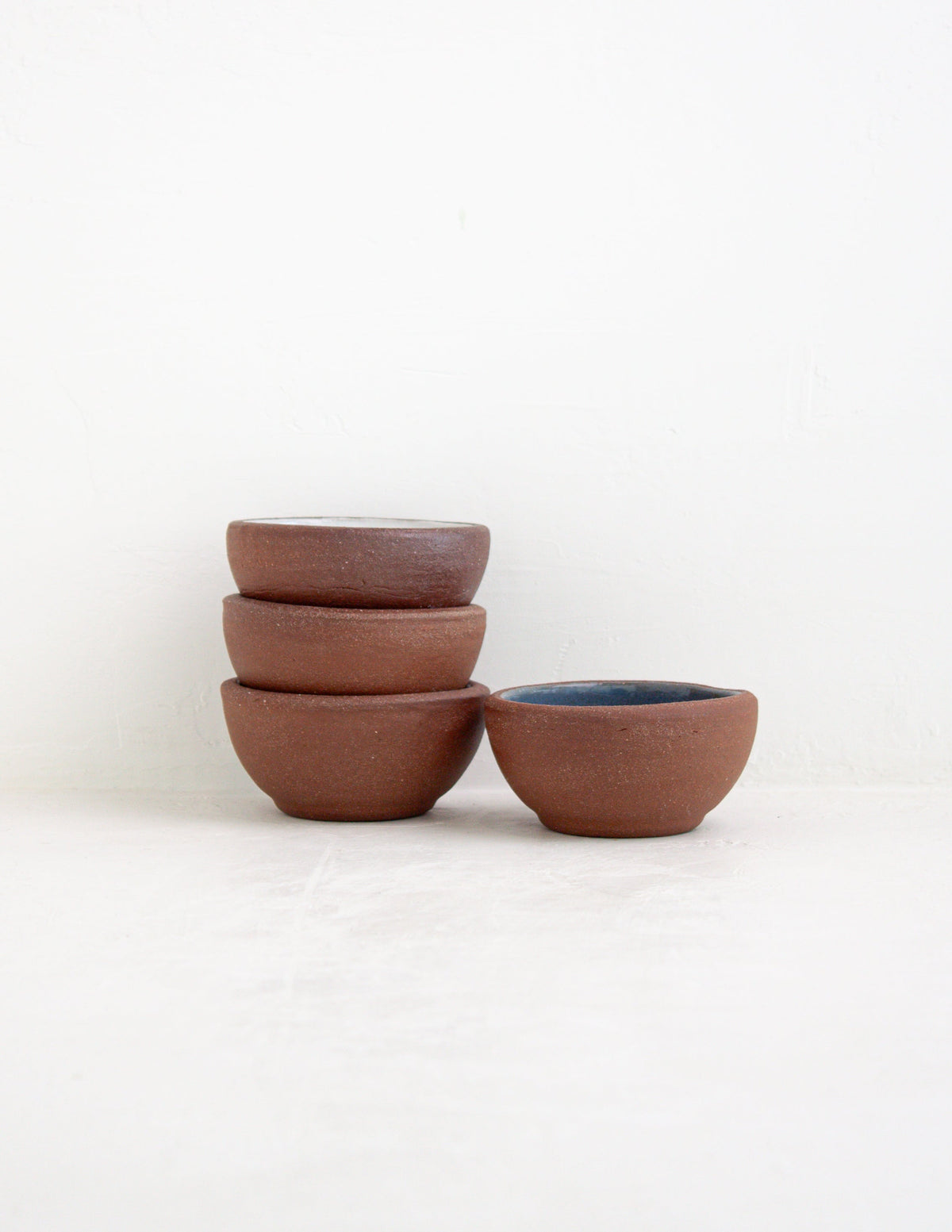 Three stacked hand-thrown stoneware sauce bowls in red clay next to one with a sky blue glazed interior