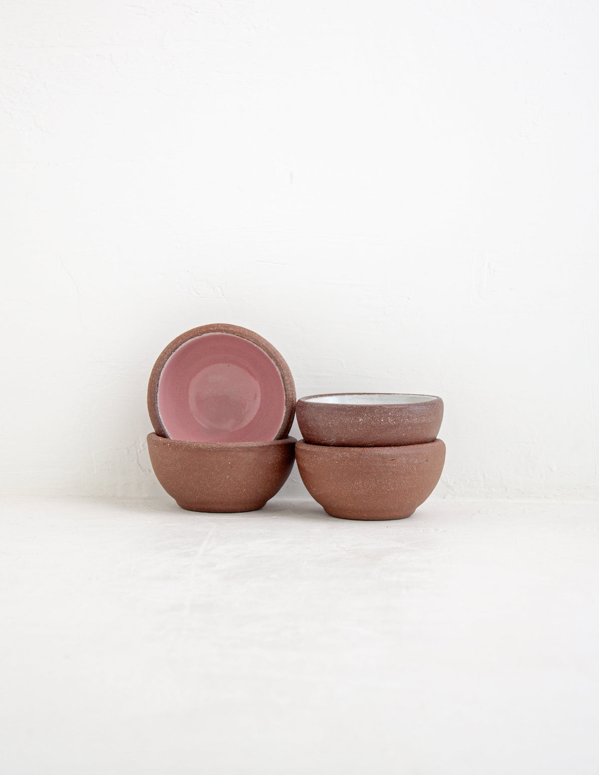 Hand-thrown stoneware coupe sauce bowls stacked and tilted, showing pink and white glazed interiors