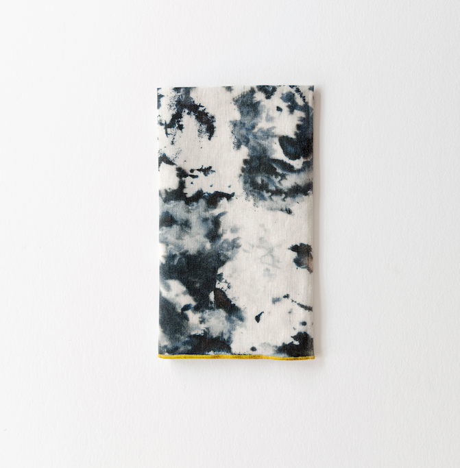 Grey marble print linen napkin folded into a rectangle with a gold edge along the bottom