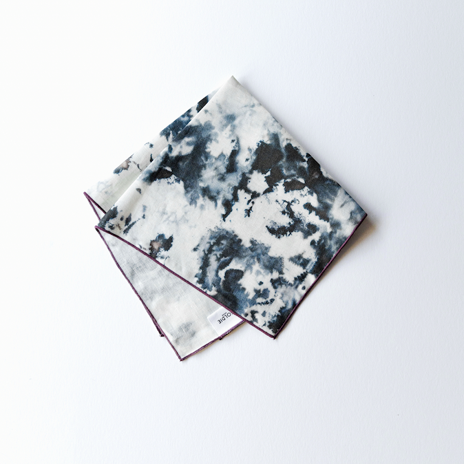 Grey marble print linen napkin with a slim plum edge, folded loosely on a white surface from above