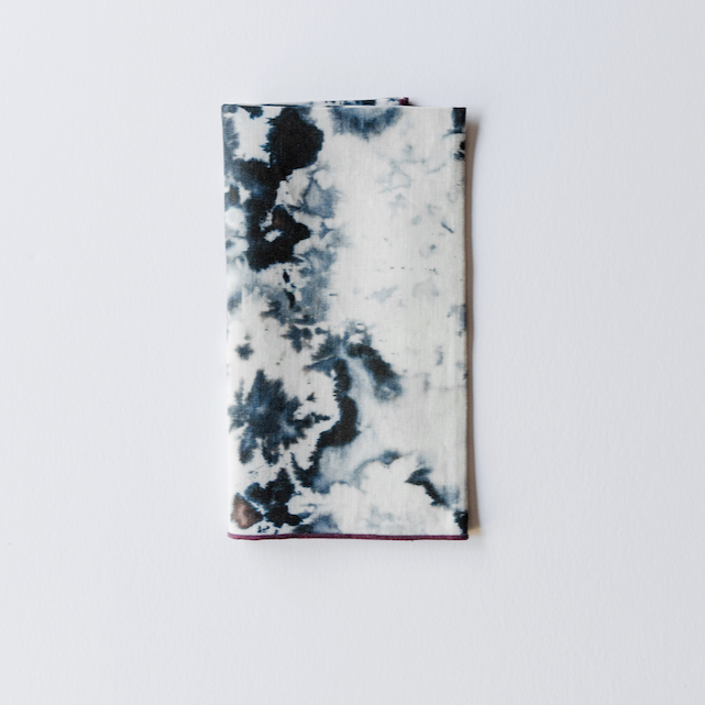 Grey marble linen napkin folded into a long rectangle with a plum edge, showing the inky print