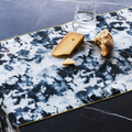 Grey marble print linen table runner with a water glass, cheese and bread on a black marble table