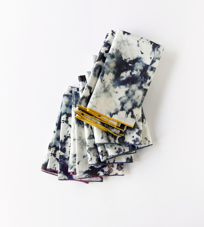 Stack of folded grey marble linen napkins with gold and plum edges fanned out on white