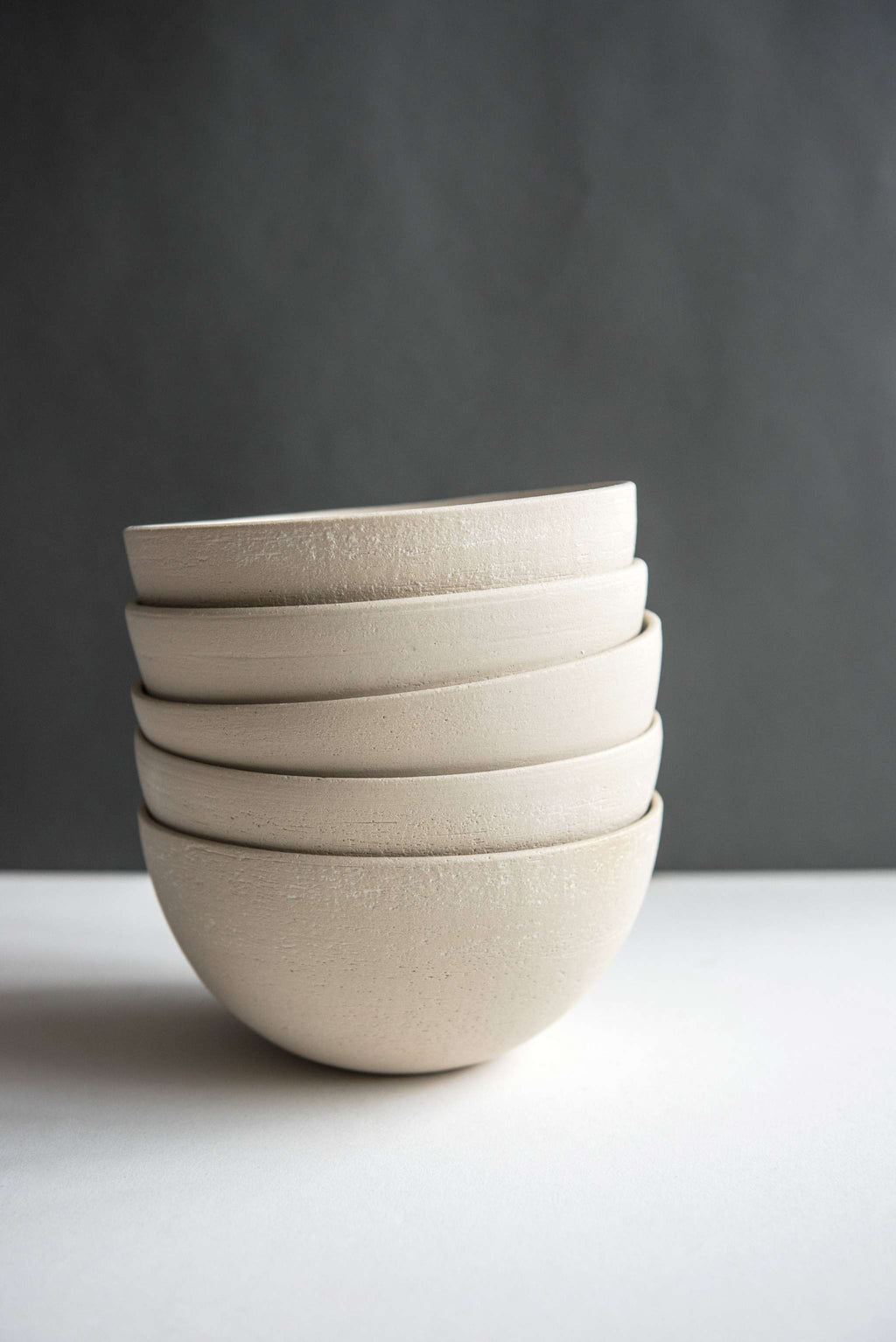 Five stoneware soup bowls with exposed sandy clay exteriors stacked straight against a charcoal backdrop