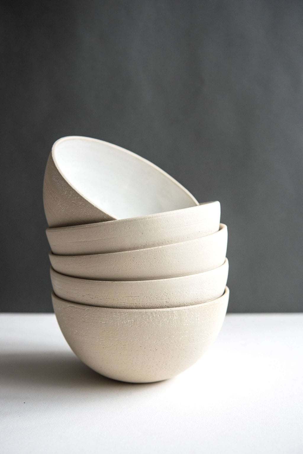 Stack of five exposed clay stoneware soup bowls with the top bowl tilted to show its white glazed interior