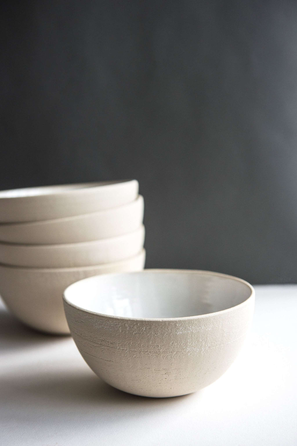 Low side view of an exposed clay stoneware soup bowl showing the textured exterior, four more stacked behind
