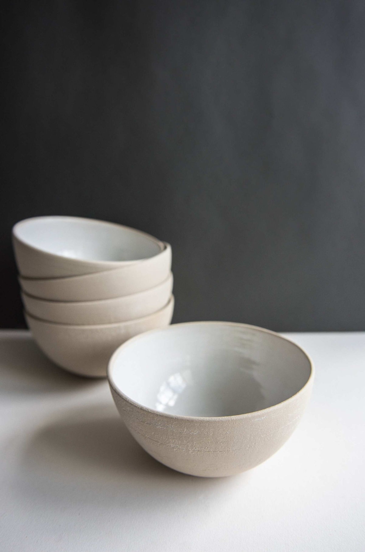 Exposed clay stoneware soup bowl with white glaze inside, set ahead of a leaning stack on a white tabletop