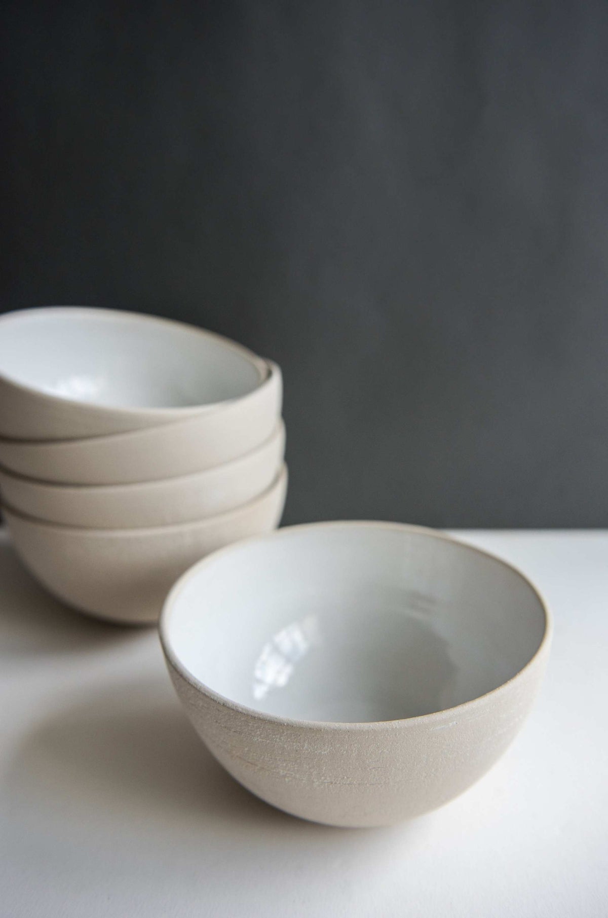 Stoneware soup bowl with exposed clay exterior and glossy white glazed interior in front of a stack of four bowls