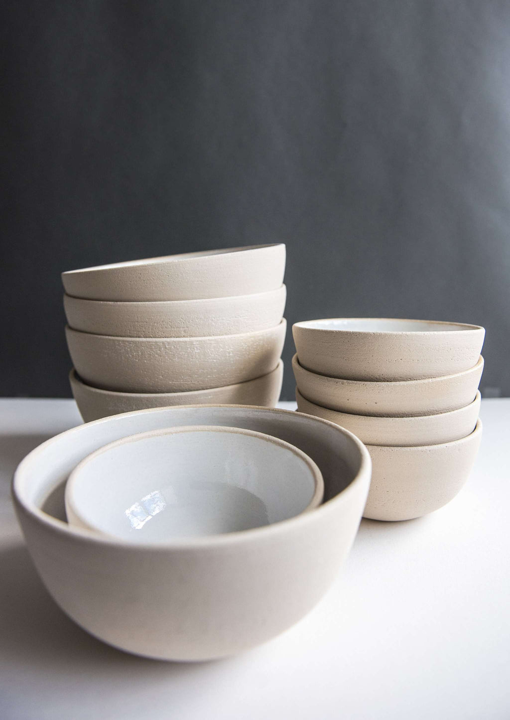 Exposed clay stoneware bowls in three sizes, two nested in front of two stacks of smaller bowls on a white table