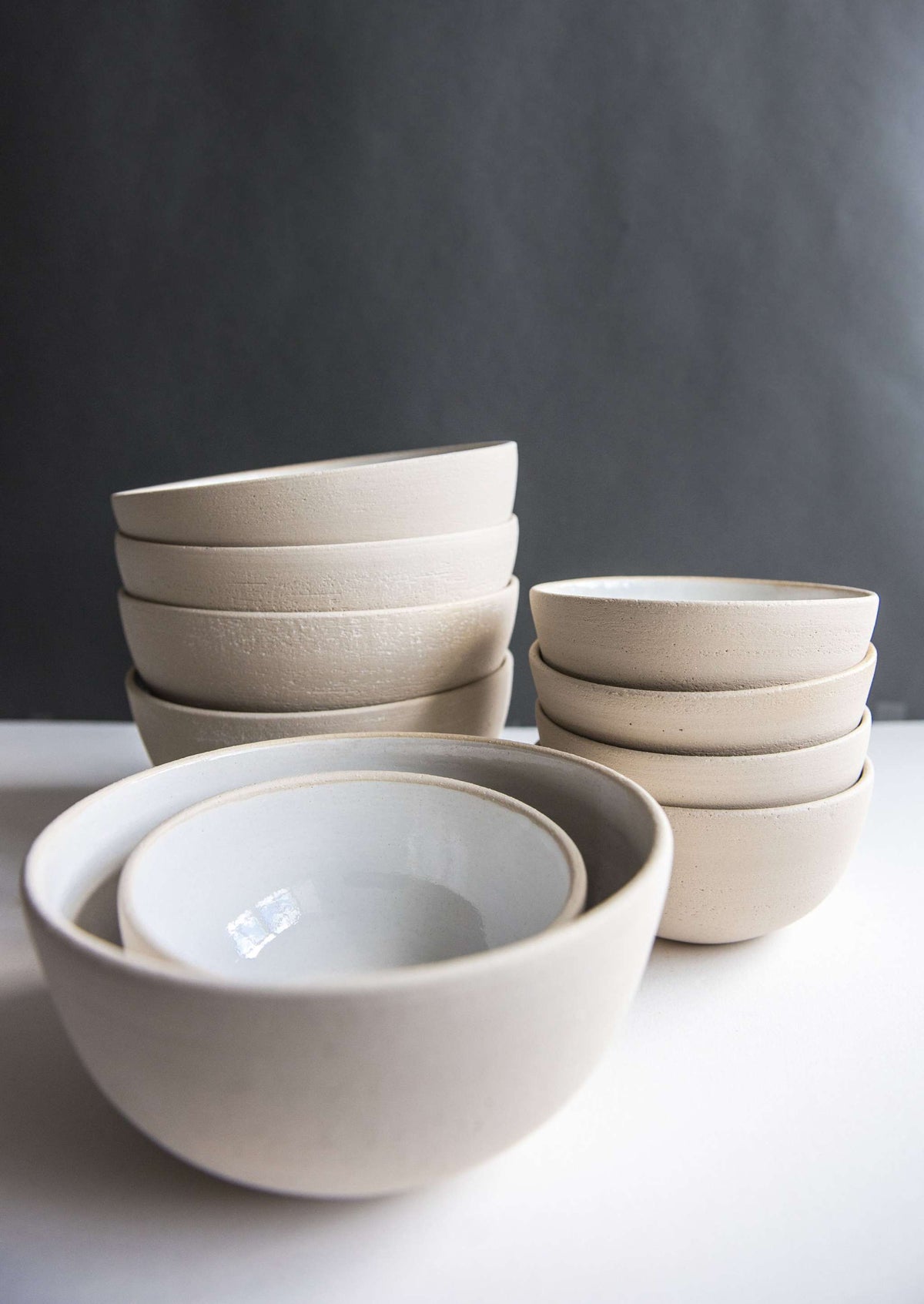 Exposed clay stoneware bowls in three sizes, two nested in front of two stacks of smaller bowls on a white table