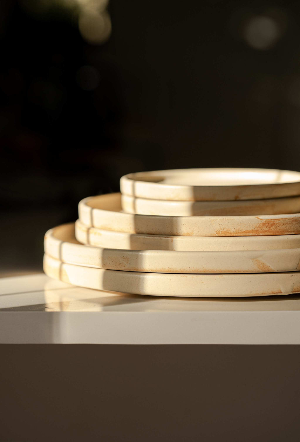 Side profile of six stacked beige matte stoneware plates with rust markings against a dark background