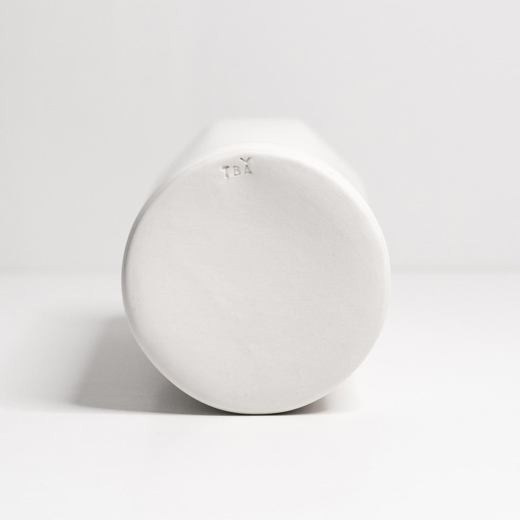 Slim white porcelain bud vase laid on its side to show the rounded base and smooth unglazed foot