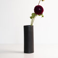 Slim Mica Black porcelain bud vase holding one deep red dahlia on a long stem against white