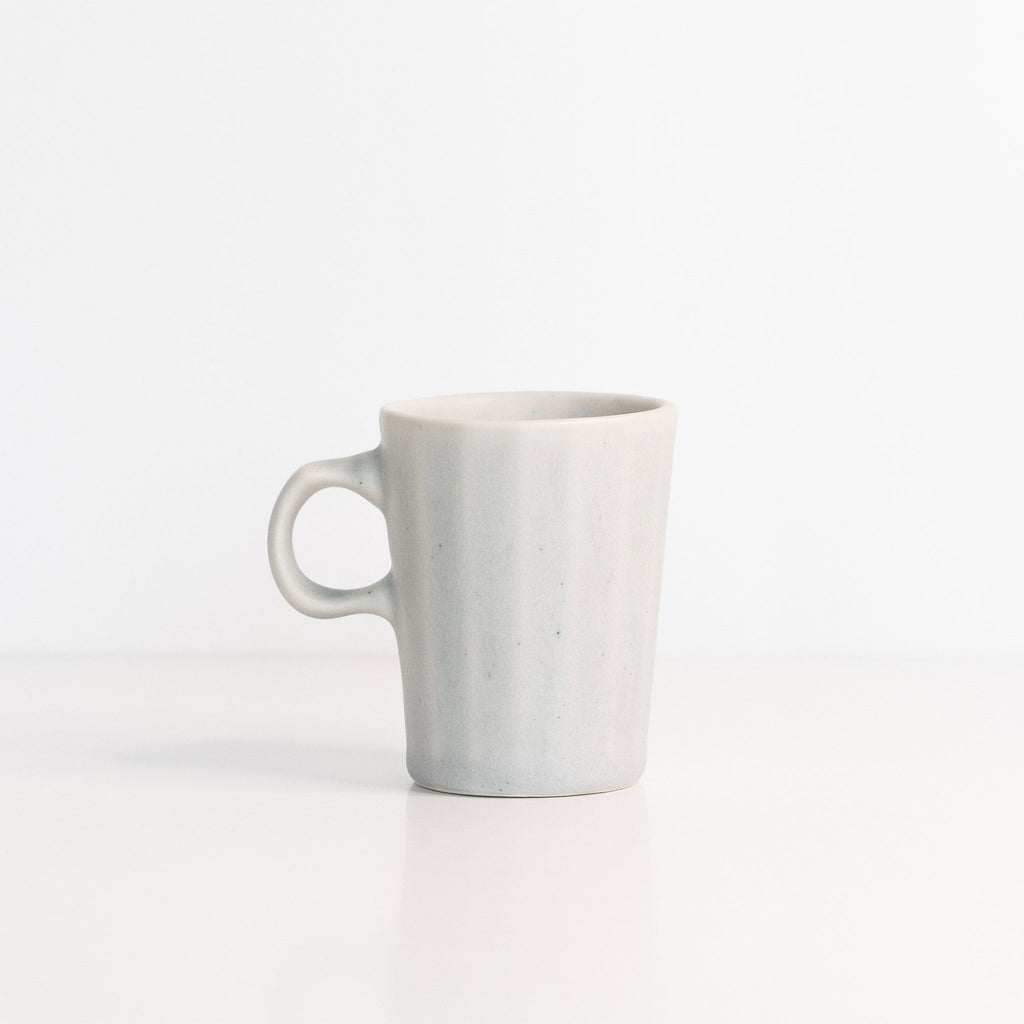 Faceted porcelain espresso cup in pale Smoke Grey with a one-finger handle on a white surface
