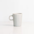Faceted porcelain espresso cup in pale Smoke Grey with a one-finger handle on a white surface
