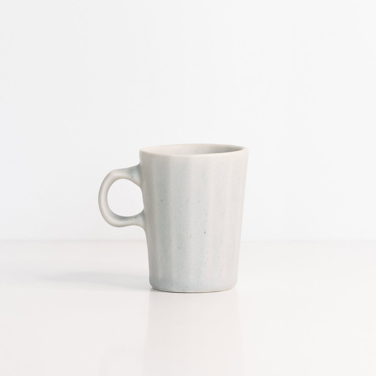 Faceted porcelain espresso cup in pale Smoke Grey with a one-finger handle on a white surface