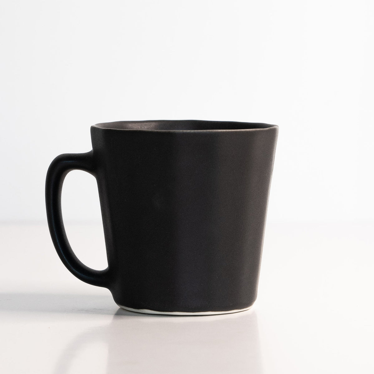Faceted porcelain coffee mug in Mica Black with a wide handle, shown on a clean white studio surface