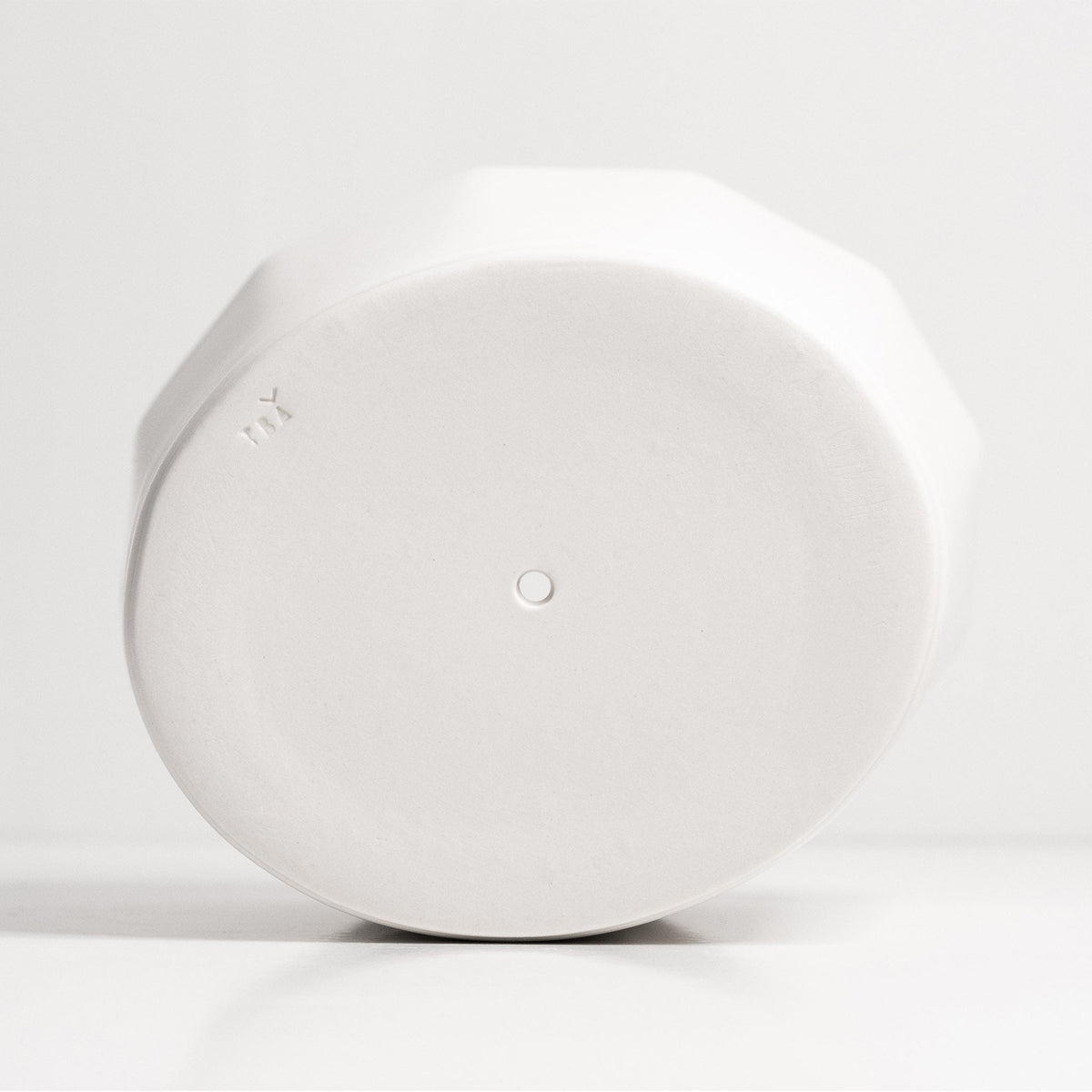 Underside of a white faceted porcelain planter showing the oval base and central drainage hole