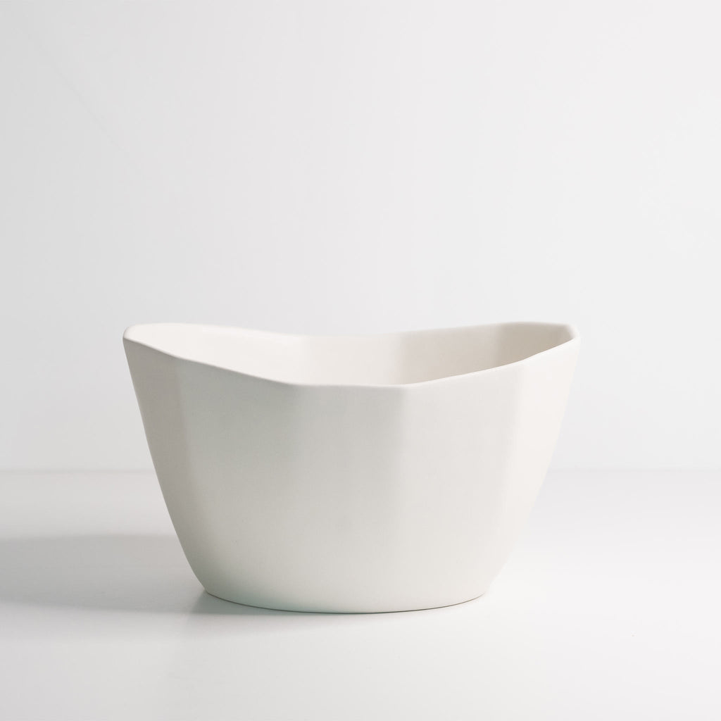 Empty medium porcelain bowl in Silk White showing the gentle wave of its oval rim from the side