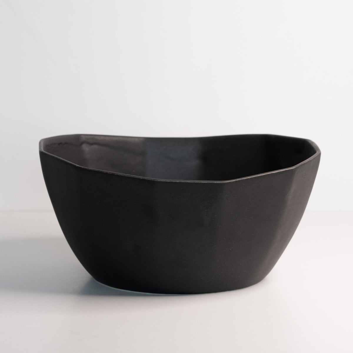 Empty large porcelain serving bowl in Mica Black, a soft wavy rim sitting over crisp faceted sides